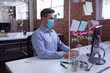 © wavebreak3 - Caucasian businessman in face mask sitting at desk with hygiene screen using computer