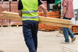 Back view of unknown man construction worker holding and carry lumber at warehouse or construction site