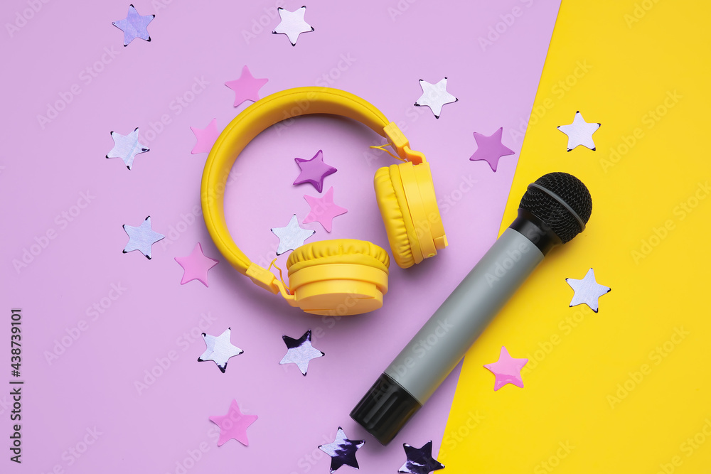 Modern microphone with headphones and confetti on color background