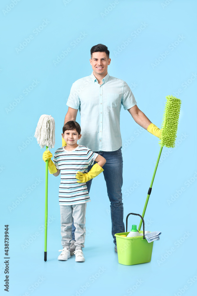 Father and son with cleaning supplies on color background