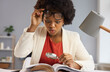 © Studio Romantic - Surprised inquisitive black woman with magnifying glass takes off glasses as she sees an amazing curious fact in the book she's reading. Shocked financial advisor studying business documents in office