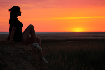 Silhouette of a girl sitting on cliff edge at sunset