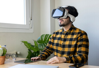 Wall Mural - man in yellow plaid shirt sitting next to a window in an office with virtual reality glasses