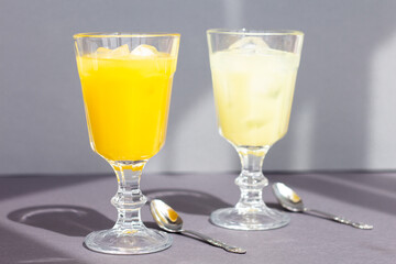 two glasses with a refreshing citrus drink or lemonade or alcoholic cocktail, a pair of casting shadows glasses isolated on grey background, minimalism