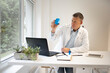 © epiximages - male chemist, scientist works at standing table and examines blue liquids in small vials and wears white coat