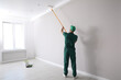 © New Africa - Man painting ceiling with roller in room, back view
