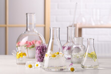 Laboratory Glassware With Flowers On White Wooden Table. Extracting Essential Oil For Perfumery And Cosmetics