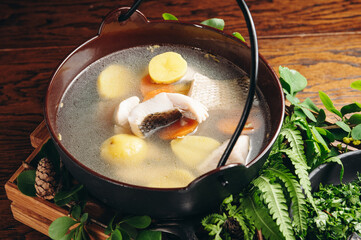 Russian traditional fish soup in a bowl - ukha, served with ember and vodka on wooden board. Fish broth. Traditional cuisine in Russia.