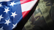 American Flag And Military Hat Or Bag. Top View Angle. Soldier Hat Or Helmet With National American Flag On Black Background. Represent Military Concept By Camouflage Object And USA Nation Flag. 