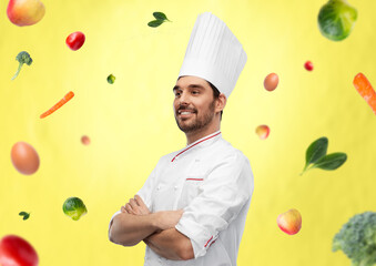 Wall Mural - cooking, culinary and people concept - happy smiling male chef in toque and jacket with crossed arms over vegetables on illuminating yellow background