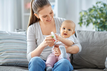 Wall Mural - family, motherhood and people concept - happy smiling mother and little baby playing with rattle at home