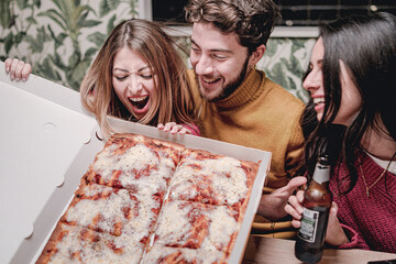 Group of young people having fun together holding a pizza cardboard box and joking together at home having a party