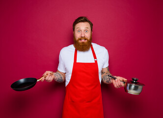 Wall Mural - afraid chef with beard and red apron cooks with pan and pot