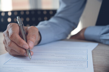 Wall Mural - Business man hand with a pen signing contract, paper document on table in office, close up