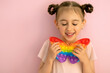 A beautiful cute little girl with her eyes closed holds a butterfly-shaped popit toy in her hand. Funny pigtails for girls . These are children's entertainment and educational toys.  Pop it toy