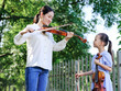 © eastfenceimage - The female teacher instructs the girl to play the violin in the outdoor park