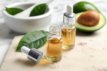 Bottle of essential oil, pipette and fresh avocado on table, closeup