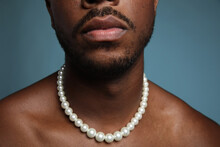 Cropped Portrait Of Shirtless Black Man With Pearl Necklace Over Blue Wall.