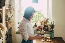 Beautiful Florist Arranging Bouquet Of A Dry Flowers At Her Workshop
Young Talented Woman Cutting With Scissors Dried Plants And Flowers Arrangement In Her Flower Shop, Sustainable Lifestyle Concept.