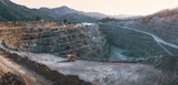 Fototapeta  - Gravel quarry with terraces, piles of stone and red crusher machine. Panorama with mountains background in twilight