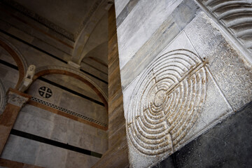 Cathedral of Lucca (Tuscany, Italy). Detail of the ancient famous maze column on the facade, decorated with a medieval labyrinth over the white marble of the church 