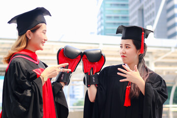 Two happy graduated women students warming square academic hat cap with red boxing gloves or mitt punch, the metaphors about life: life is a fight for territory after celebrating successful education 