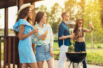 Wall Mural - Young friends have fun frying meat, enjoying barbecue, with drinks, on a sunny day in nature