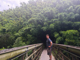 Fototapeta Miasto - Man Standing on Bridge on Jungle Path