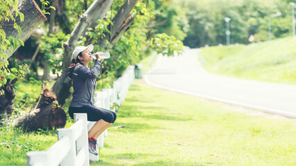 Wall Mural - Healthy athletic asia woman is drinking pure water from the bottle refreshing herself after exercise in the nature park. Healthy and Lifestyle Concept, copy space for banner