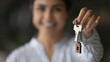 New home. Blurred portrait of smiling young female seller realtor broker holding key in hand giving you client customer buyer renter after making successful deal. Soft focus on bunch of keys. Close up