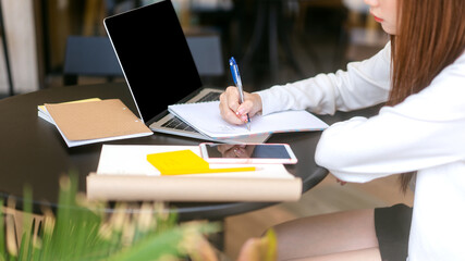 Wall Mural - Young adult women hand writing note for study and work online at cafe table with laptop.