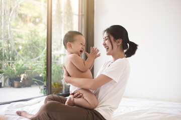 asian mom smiling happy holding and playing clap hand with her son. mom and baby in mother’s day con