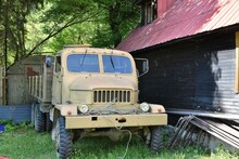 An Old All-terrain Multi-purpose Truck The Praga V3S, Produced Since 1953 In Czechoslovakia, Abandoned In The Countryside Near Village House And Green Bushes And Trees. 