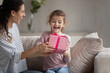 © fizkes - Smiling young Latin mom give wrapped gift box to excited small biracial daughter congratulate with birthday. Happy loving Hispanic mother make surprise present to overjoyed ethnic girl child at home.