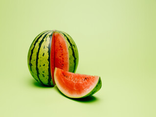 Wall Mural - Fresh and juicy watermelon with a cut slice isolated on a pastel green background. Summer healthy refreshment. Creative tropical fruit or vegetable food concept.