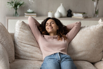 Wall Mural - Smiling millennial Hispanic woman lying relaxing on couch at home sleep or take nap daydream. Happy young Latino female renter rest on sofa in living room breathe fresh ventilated condition air.