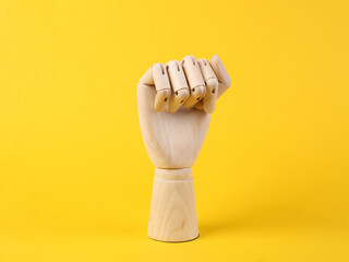 Wooden hand shows a fist gesture on a yellow background. Feminism symbol