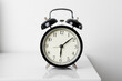 © Rattanachat - black alarm clock on white table. morning time.