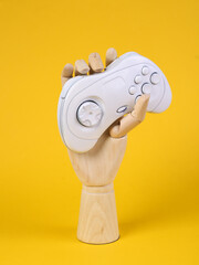 Canvas Print - Wooden hand holding white gamepad on yellow background