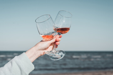 Wall Mural - Two glasses of rose wine in female hands against the sky and seashore.