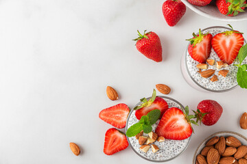 Wall Mural - Vegan breakfast. Chia pudding in glasses with fresh strawberries, nuts and mint on white background. top view