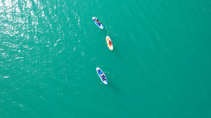 Wall Mural - A group of people ride sup surfing in the lake. Aerial view from the drone of the green water and rocky beaches. Inflatable sapboard board. Trees and bushes grow on the bank of Kapchagai.