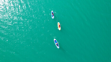 Wall Mural - A group of people ride sup surfing in the lake. Aerial view from the drone of the green water and rocky beaches. Inflatable sapboard board. Trees and bushes grow on the bank of Kapchagai.