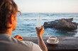 Anonymous caucasian man holding a glass of milkshake at a beach bar on the ocean shore. Idyllic lifestyle scene at restaurant on seaside.