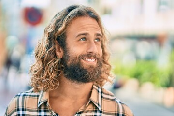 Wall Mural - Young caucasian man with long hair smiling happy at the city.