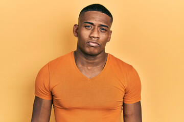 Young black man wearing casual orange t shirt with serious expression on face. simple and natural looking at the camera.