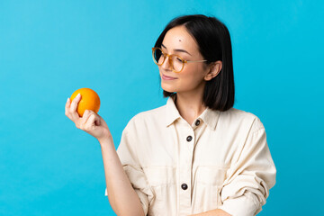 Wall Mural - Young caucasian woman isolated on blue background holding an orange