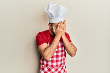 Wall Mural - Young hispanic man wearing baker uniform with sad expression covering face with hands while crying. depression concept.