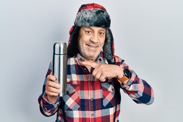 Sticker - Handsome mature handyman wearing winter hat with ear flaps holding thermo smiling happy pointing with hand and finger