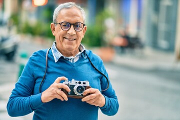 Wall Mural - senior grey-haired tourist man smiling happy using vintage camera at the city.